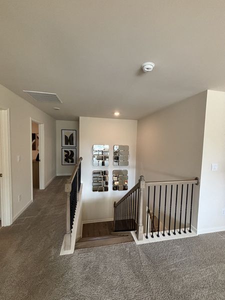 A cozy carpeted landing area with modern wall art and elegant stair railing inviting you to explore further.