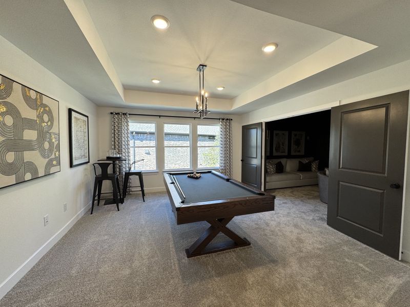 A stylish game room featuring a sleek pool table, plush carpeting, and modern art, perfect for entertainment and relaxation.