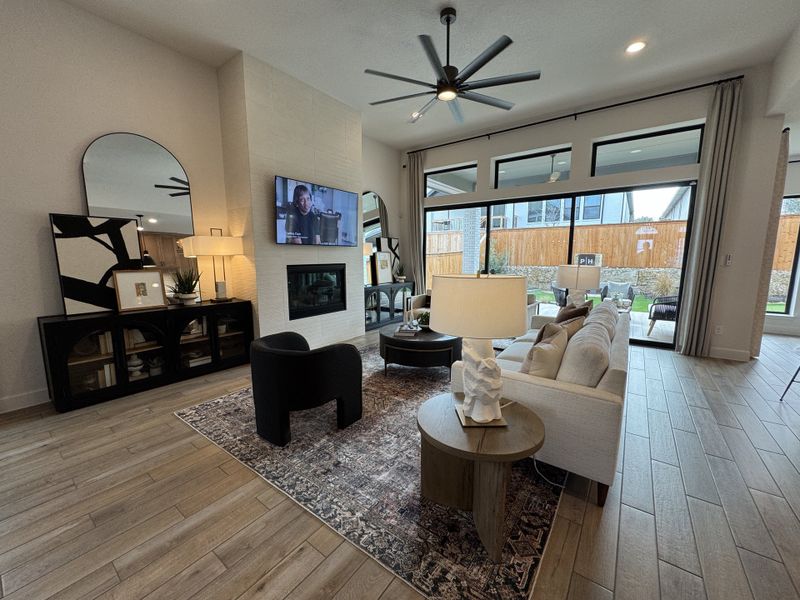 A spacious living room with a sleek fireplace, large windows, and modern furniture, featuring stylish decor and warm wood flooring.