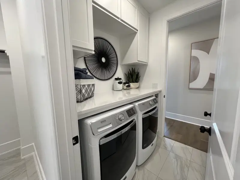 A modern laundry room featuring sleek cabinetry, top-load appliances, and decorative elements enhancing its functionality.