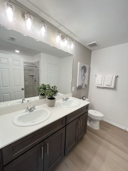 A modern bathroom with double sinks, dark cabinets, bright overhead lighting, and minimalist decor. A modern bathroom with double sinks, dark cabinets, bright overhead lighting, and minimalist decor.