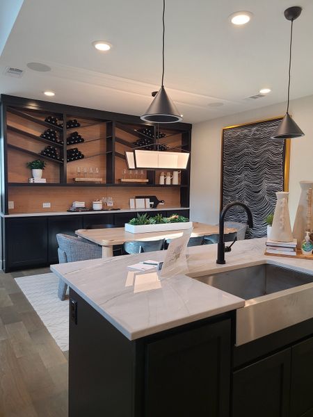 A modern kitchen with sleek black cabinetry, open shelving, stylish pendant lights, and a chic dining nook.