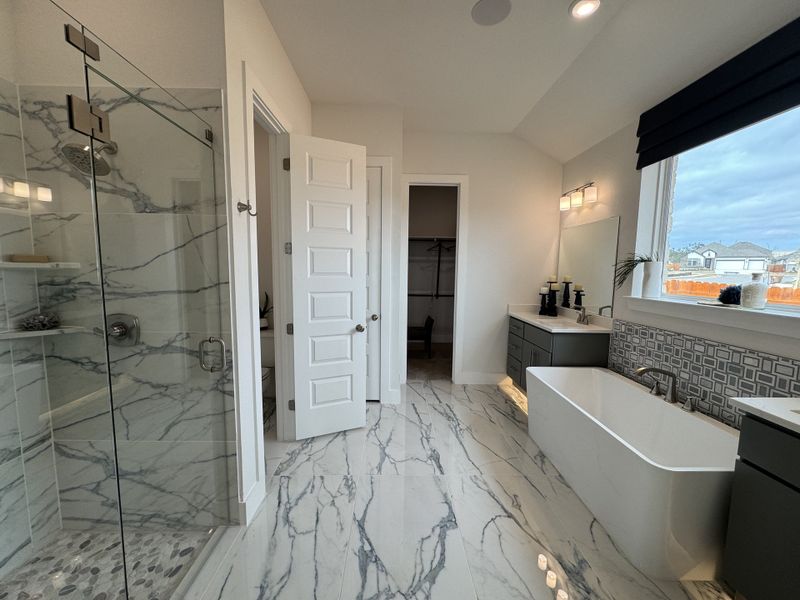 A luxurious bathroom with a marble shower, freestanding tub, sleek vanity, and large window for natural light.