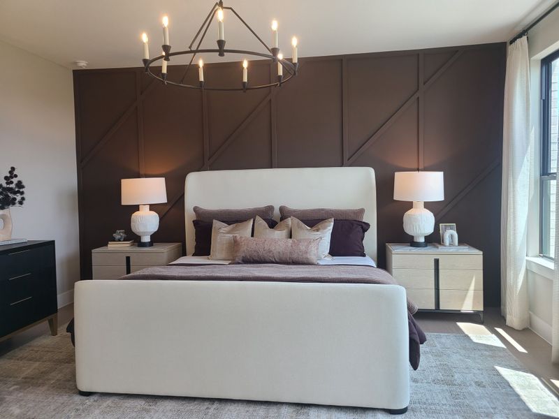 A chic bedroom featuring a plush bed with layered pillows, sleek side tables, and a geometric chandelier.