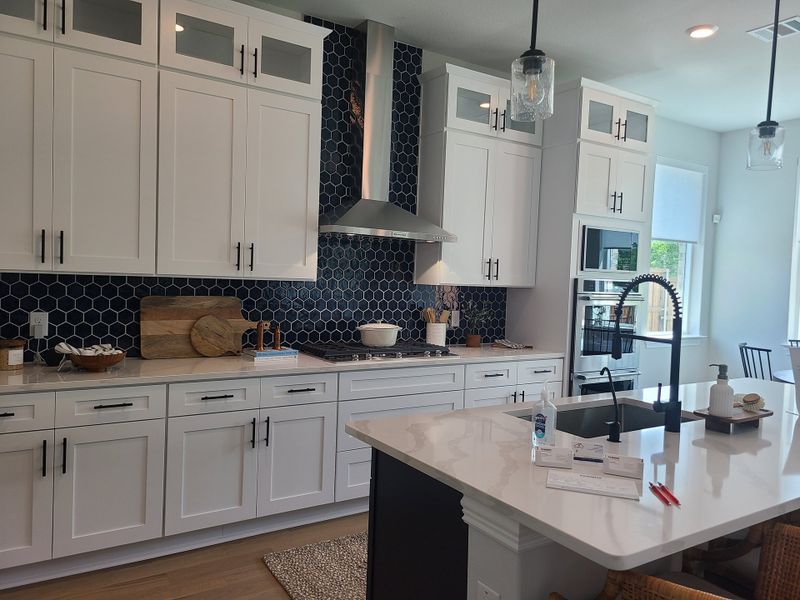 A modern kitchen featuring white cabinetry, a dark hexagonal tile backsplash, and a sleek island with a large faucet.
