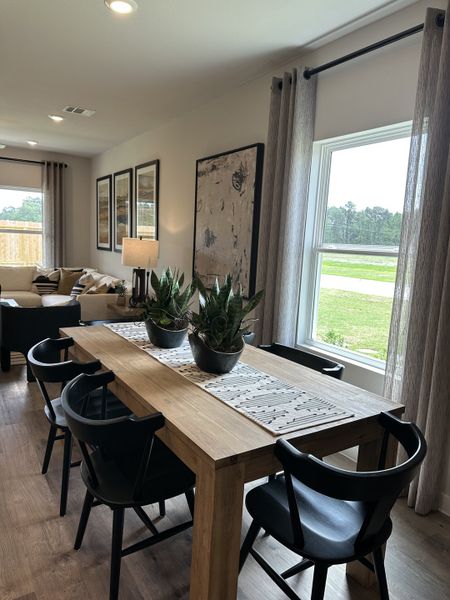 A cozy dining area with a wooden table, black chairs, and large windows offering natural light.