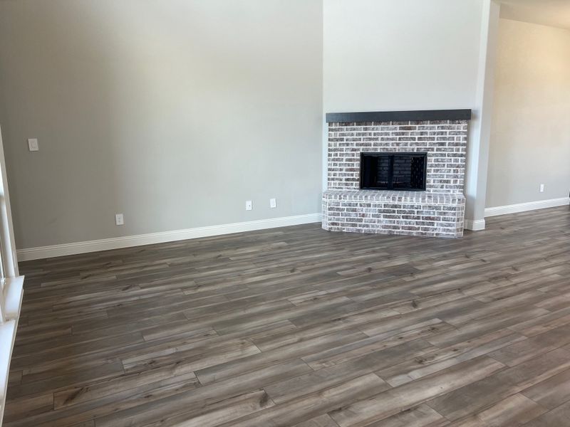 A modern living area with gray wood flooring, a white brick fireplace, and soft neutral walls.