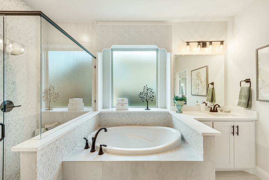 Master bathroom with soaking tub, glass shower, white vanity cabinets, and mosaic tile surround near frosted window Master bathroom with soaking tub, glass shower, white vanity cabinets, and mosaic tile surround near frosted window