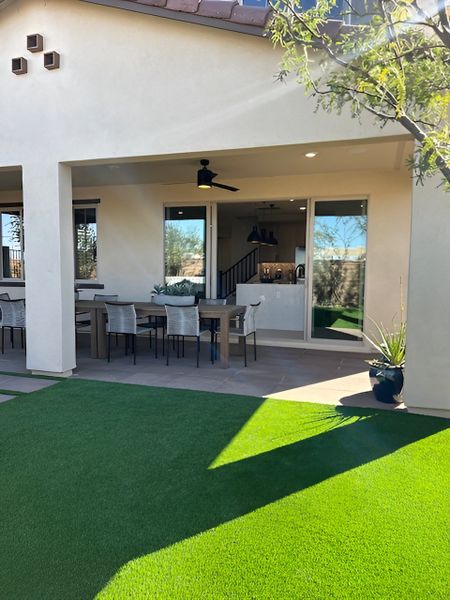 A covered patio with a dining area, artificial turf, and a view of the open-concept indoor living space.