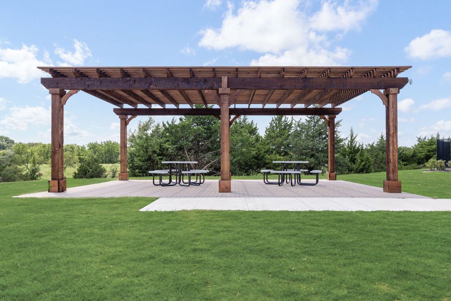 Large wood pergola with lattice roof over a paved patio with two picnic tables on a grassy lawn