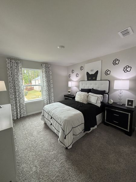 A cozy bedroom featuring a chic black-and-white theme with decorative cat artwork and plush carpeting.