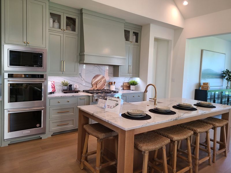 A modern kitchen with sage green cabinets, stainless steel appliances, and a large island with woven stools and elegant accents. A modern kitchen with sage green cabinets, stainless steel appliances, and a large island with woven stools and elegant accents.