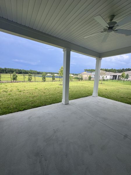 A spacious covered patio with a ceiling fan overlooking a green yard and open fence, perfect for relaxation.