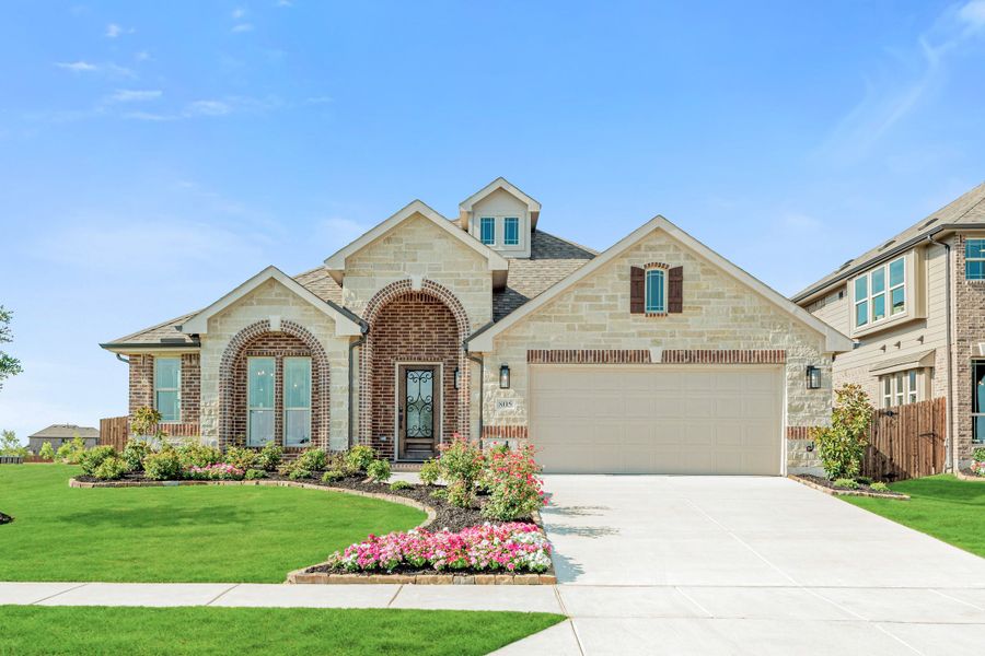 Single-story home with brick and stone exterior, arched entry, two-car garage, and landscaped front yard with flowers