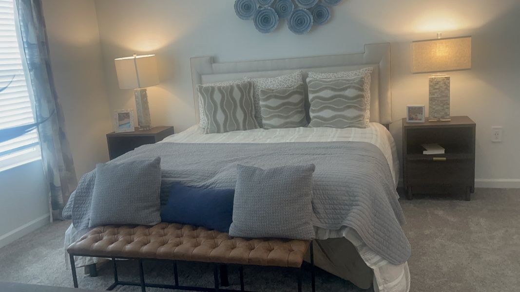A cozy bedroom with a tufted bench, elegant lamps, layered bedding, and decorative pillows creating a serene ambiance.