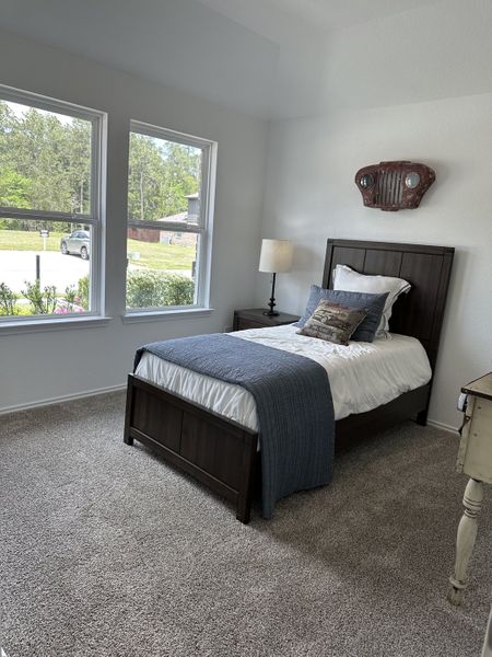A cozy bedroom with plush carpet, twin bed, and large windows offering lovely natural light. Simple decor adds charm.