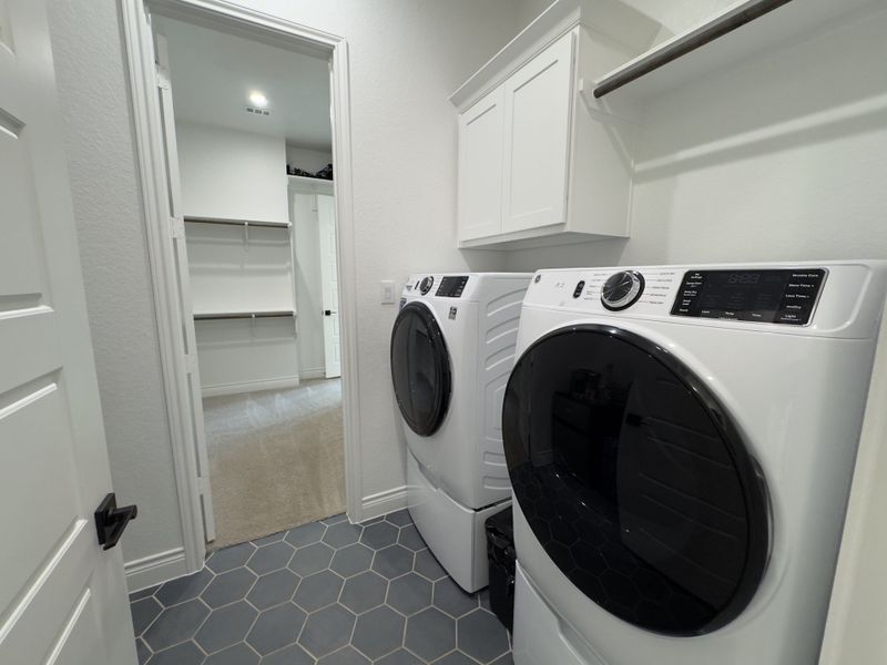 A modern laundry room with sleek appliances, hexagonal tile flooring, and white cabinetry leading to a spacious closet.
