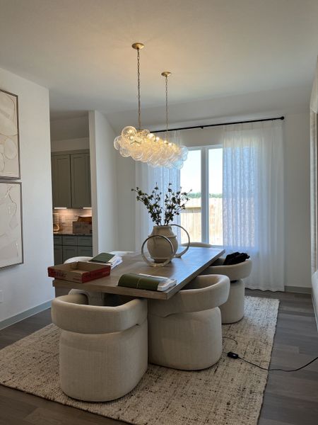 A modern dining room with elegant chairs, a wooden table, and a sculptural light fixture, bathed in natural light.