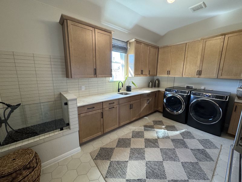 A modern laundry room with sleek cabinets, black appliances, and a geometric rug for a contemporary touch.