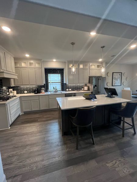 A modern kitchen featuring sleek cabinetry, dark backsplash, and a spacious island with elegant pendant lighting.