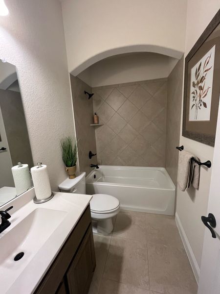 A cozy bathroom with a sleek vanity, tiled bath, arched ceiling, and elegant decor in neutral tones.