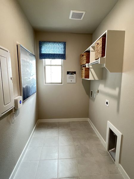 A functional laundry room with tiled flooring, a window with a blue shade, and storage shelves with woven baskets.