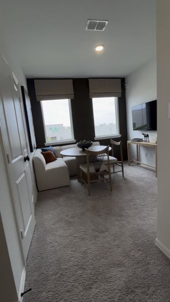 A cozy living room with plush carpet, a round table, modern seating, and wall-mounted TV for a relaxed ambiance.