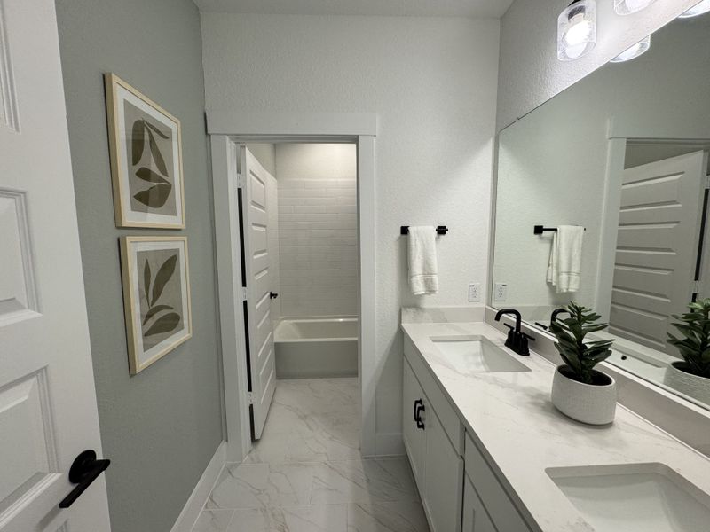 Modern bathroom featuring dual sinks, sleek black fixtures, and elegant decor with framed botanical art.