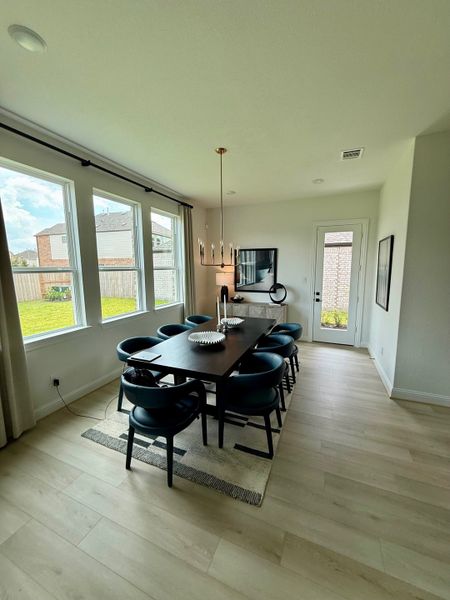 A chic dining room with wood flooring, modern lighting, and large windows, creating a bright and inviting space.