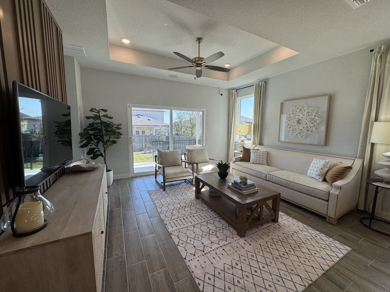 Elegant living room with a tray ceiling, wooden accents, and cozy seating. Large windows invite natural light. Elegant living room with a tray ceiling, wooden accents, and cozy seating. Large windows invite natural light.