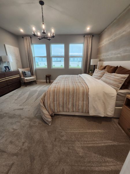 A cozy bedroom featuring modern lighting, striped bedding, and neutral tones with a plush carpet and a serene ambiance.