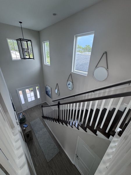 An elegant staircase with dark wood steps and a modern chandelier, featuring natural light and decorative mirrors.