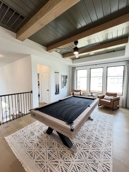 A chic game room with a sleek pool table, cozy seating, and beamed ceiling, perfect for entertainment and relaxation.