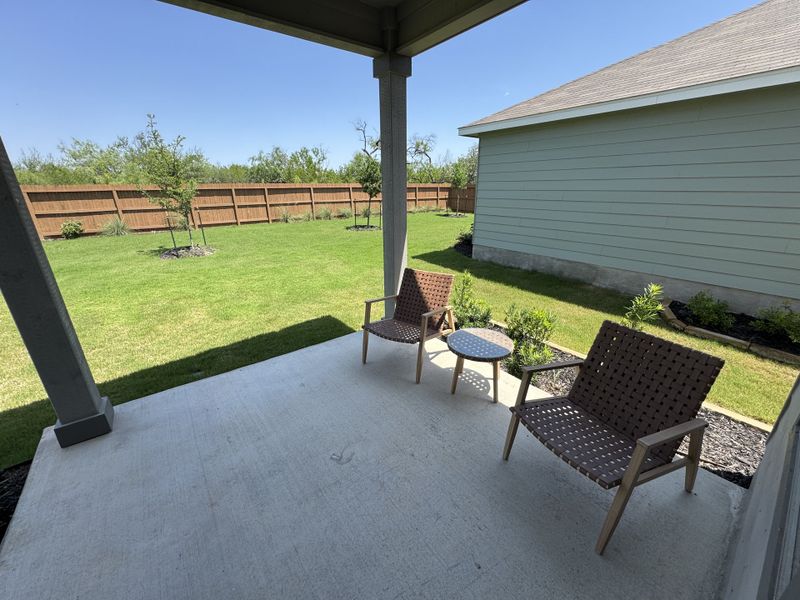 A cozy patio with woven chairs, a small table, and a lush fenced backyard perfect for relaxation and outdoor enjoyment. A cozy patio with woven chairs, a small table, and a lush fenced backyard perfect for relaxation and outdoor enjoyment.