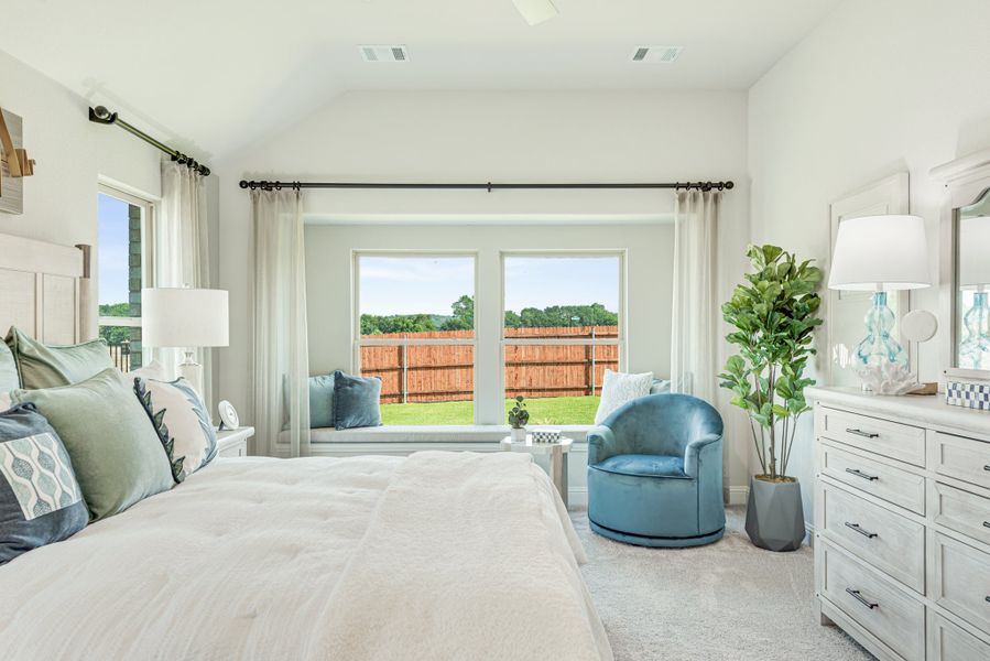 Bright master bedroom with vaulted ceiling, window seat, blue accent chair, and white dresser Bright master bedroom with vaulted ceiling, window seat, blue accent chair, and white dresser