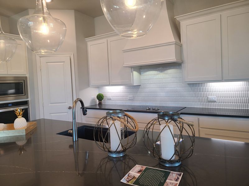 A modern kitchen featuring sleek cabinetry, textured backsplash, elegant pendant lighting, and a dark marble countertop.