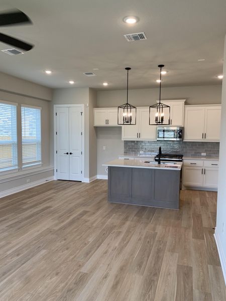 An open kitchen with sleek pendant lighting, white cabinetry, and light wood floors.