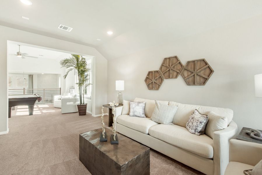 Open living area with cream sofa, wood wall decor, and game room visible through arched doorway