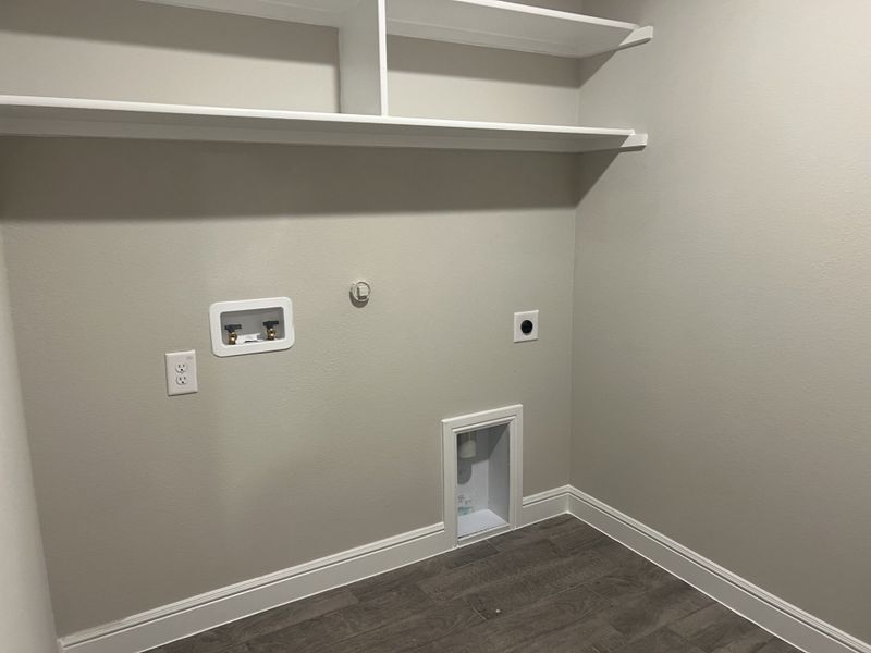 A spacious laundry room with sleek gray flooring, white shelving, and modern utility hookups. A spacious laundry room with sleek gray flooring, white shelving, and modern utility hookups.