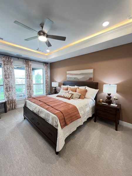A cozy bedroom with a warm color palette, tray ceiling, large windows, and elegant furnishings.