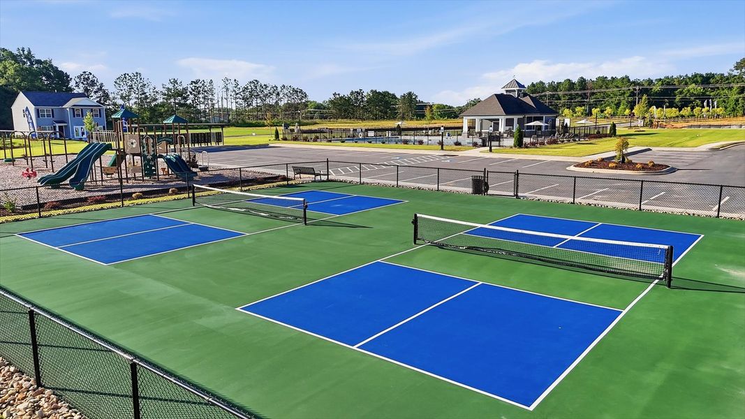 Two community fenced in pickleball courts surrounded by a spacious green field and playground at Harrier Point