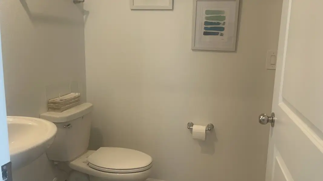 A minimalist bathroom with a sleek pedestal sink, modern toilet, and stylish artwork on the walls.