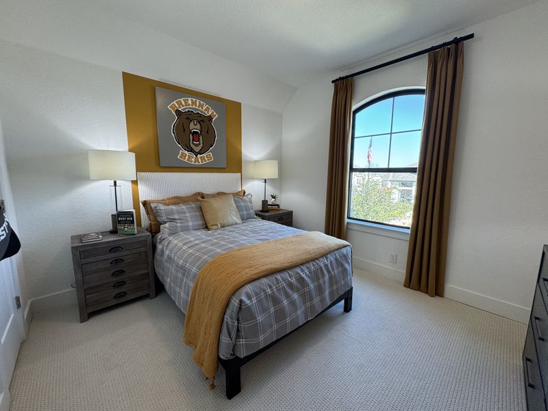 A cozy bedroom featuring a plaid bedspread, warm gold accents, and a large arched window with brown curtains. A cozy bedroom featuring a plaid bedspread, warm gold accents, and a large arched window with brown curtains.