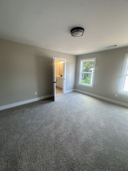A cozy bedroom with plush carpeting, neutral walls, and natural light from a large window opening to an ensuite bathroom. A cozy bedroom with plush carpeting, neutral walls, and natural light from a large window opening to an ensuite bathroom.