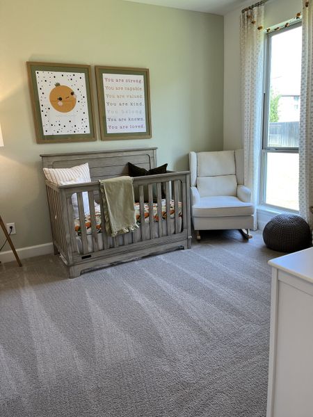 A cozy nursery featuring a gray crib, soft armchair, and uplifting artwork, bathed in natural light from a large window.