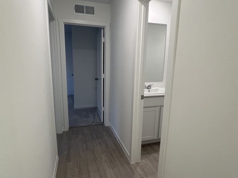 A minimalist hallway with wooden floors, white walls, and a glimpse of a bathroom vanity in a modern home.