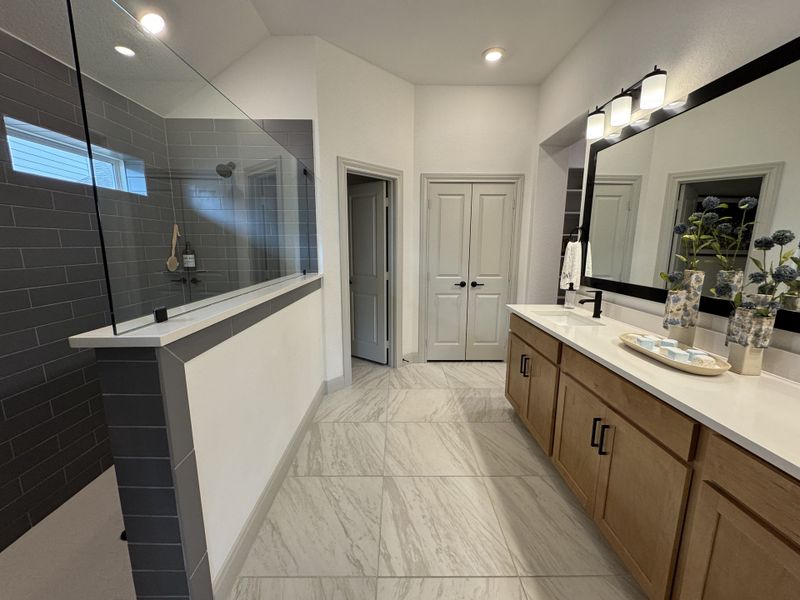A modern bathroom with a large mirror, sleek vanity, and spacious walk-in shower with gray tile accents.