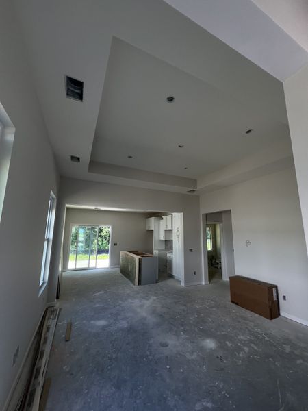 An open-concept room with high tray ceilings, large windows, and a partially constructed kitchen offering ample natural light.