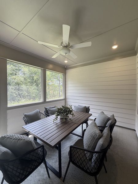 A cozy screened-in porch with a sleek wooden table, plush chairs, and a ceiling fan for tranquil outdoor dining.