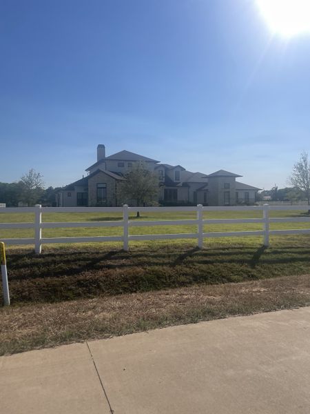 A modern estate with a white fence and expansive grounds in Tealpointe Lake Estates by Jamestown Estate Homes (Tomball, TX).